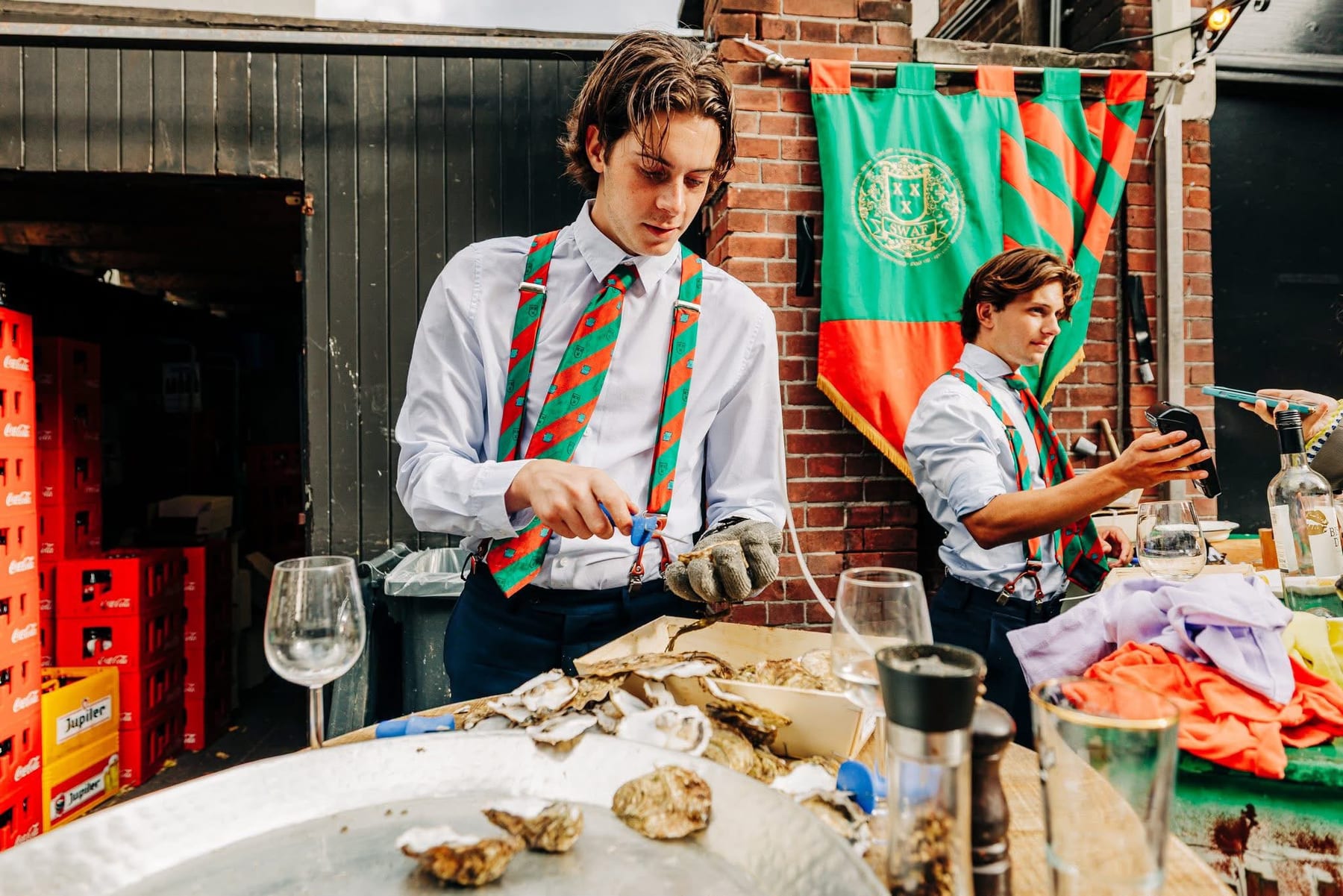 Een lid opent een oester voor de groen-rode SWAF-vlag met clubwapen.